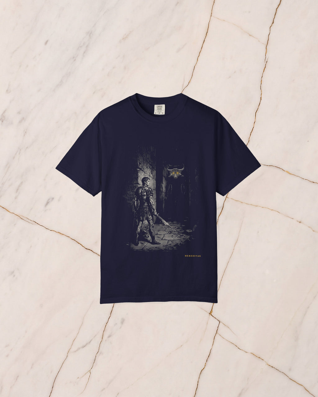 The THESEUS t-shirt in True Navy, laid flat on pale marble. Theseus in the labyrinth corridor with his sword held low, and the Minotaur waiting in the dark ahead, horns catching the light and eyes burning gold.