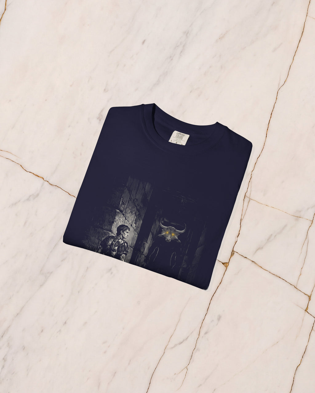The THESEUS t-shirt in True Navy, folded on pale marble, showing the weight of the cotton and the detail of the bone-line print.