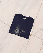 The THESEUS t-shirt in True Navy, folded on pale marble, showing the weight of the cotton and the detail of the bone-line print.