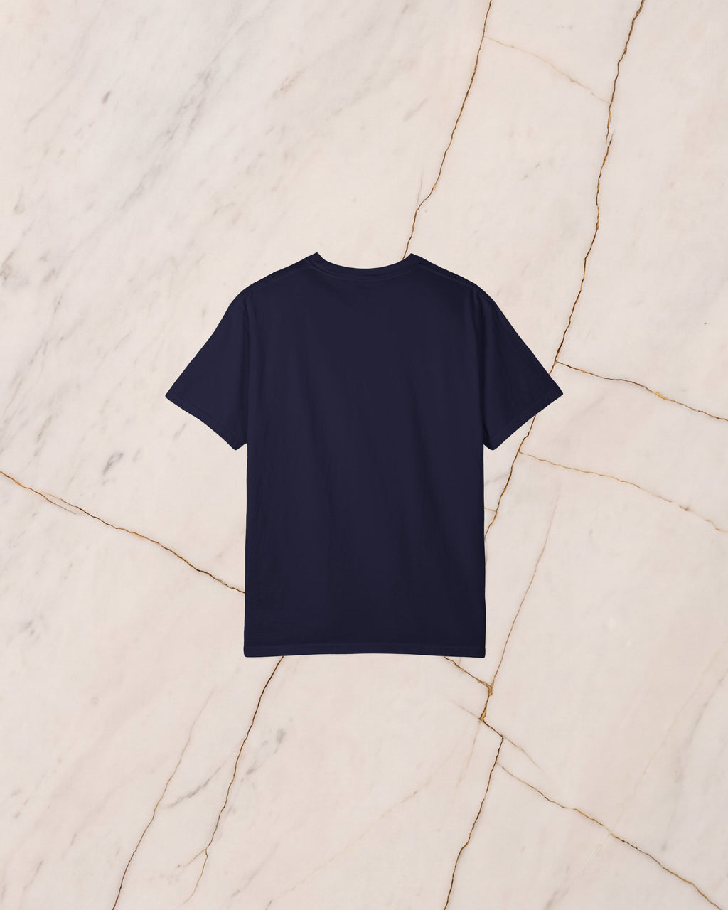The back of the THESEUS t-shirt in True Navy, unprinted, laid flat on pale marble.