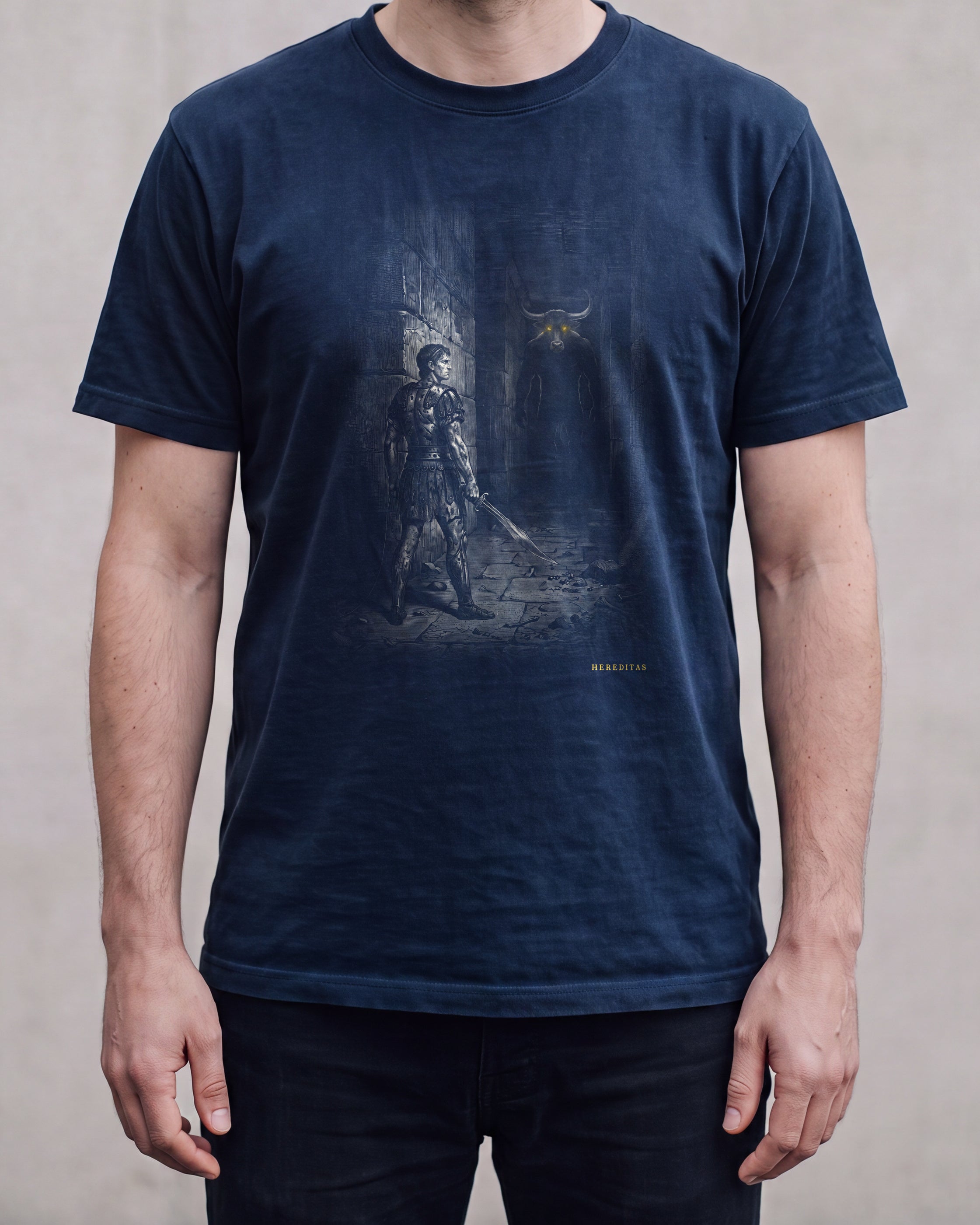 The THESEUS t-shirt in True Navy shown worn, cropped to the torso against a plain concrete wall, so the drape of the cotton and the scale of the chest print can be judged.