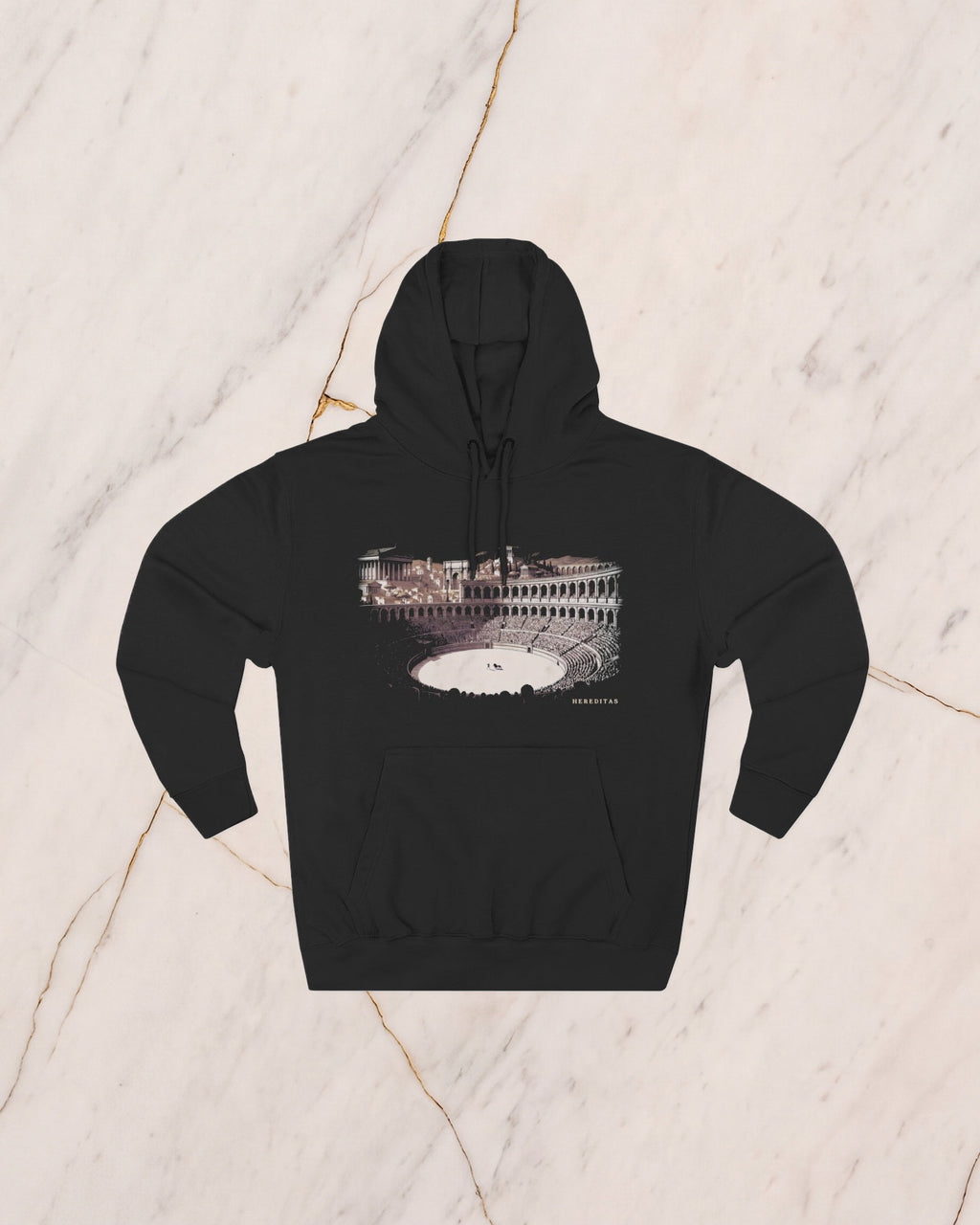 The VENATOR hoodie in black, laid flat on pale marble. A hunter and a lion alone on the arena sand, the temples of the city rising beyond the wall, drawn in bone line and lit by a low sun.